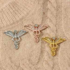 Drei Caduceus Medizinnadeln mit Engelsflügeln und Strass auf beige gestricktem Pullover