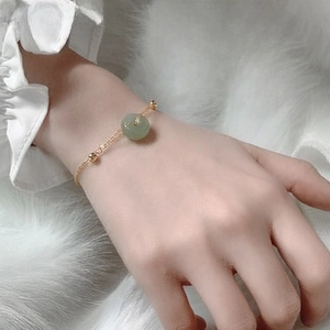 Macro shot of gold chain bracelet featuring a green jade donut charm on a soft plush background