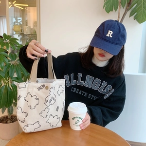 White corduroy bear tote bag being held by a model in a cozy cafe setting