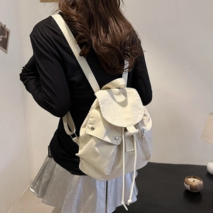 Detail of cream white oxford nylon backpack featuring drawstring closure and flap pockets