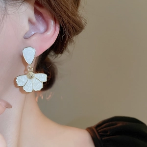 Close-up of white enamel flower earring with gold pistil detail on model ear