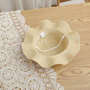 Détail du chapeau de paille enfant montrant l'étiquette 52cm et le bord ondulé sur dentelle