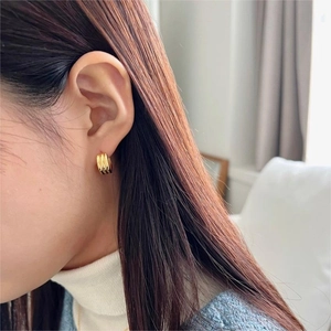 Close-up of elegant gold triple-layered hoop earrings worn by a model in a cozy setting