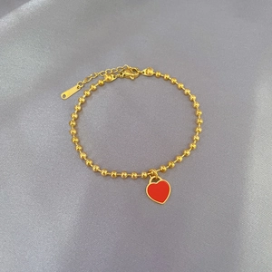 Detailed macro view of a golden stainless steel bead bracelet featuring a red heart pendant