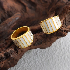 Golden wide band rings with white shell inlay on rustic wood background for women