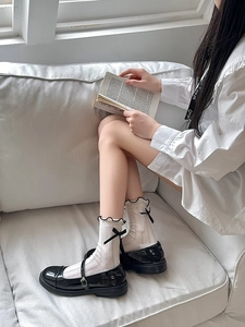 Detail of beige ruffle socks with black bows paired with glossy Mary Jane shoes