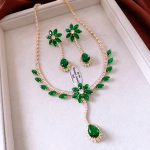 Detailed macro view of the gold flower pendant necklace and earrings with emerald gems
