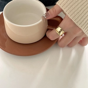 Detail of irregular textured gold wave ring worn while holding a coffee cup