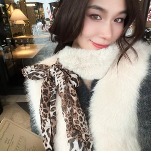 Detail of soft white faux fur scarf featuring a bold leopard print satin bow tie accent