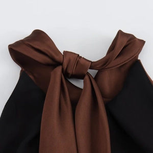 Detail of the halter neckline featuring a dark brown satin bow tie on a black dress