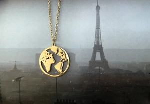 Close-up of gold hollow world map necklace pendant on vintage Eiffel Tower background
