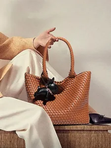Brown woven leather tote bag with French Bulldog charm shown in a minimalist lifestyle setting