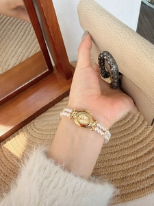 Macro detail of oval gold dial and double-strand pearl bracelet on a vintage watch