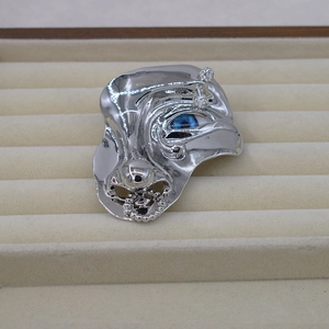 Detail of silver abstract face brooch featuring a blue eye and inlaid rhinestones
