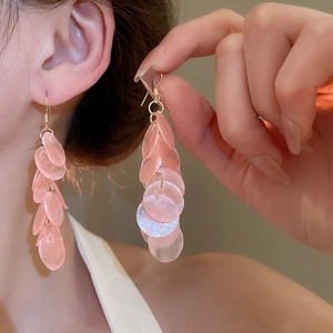 Close-up of pink shell luster tassel earrings worn by a model for a beach holiday look