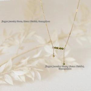 Detail of gold necklace with olive green beads and delicate hanging chains focal point