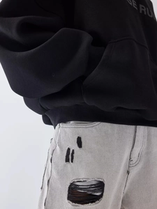 Detail of heavy black hoodie cuff and gray distressed washed jeans with ripped texture