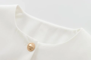 Detailed macro view of a gold relief button on a white woven textured jacket neckline