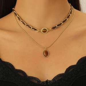 Mehrlagige Goldkette mit Tigerauge-Anhänger und Lederband auf schwarzem Spitzenkleid