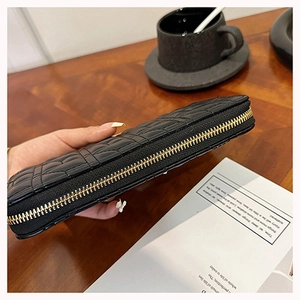 Detailed side view of black quilted long wallet with golden zipper on a wooden desk