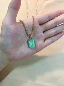 Macro detail of rectangle green emerald cut pendant on a gold twisted rope chain