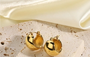 Detailed close-up of chunky gold hoop earrings on elegant silk and stone textures