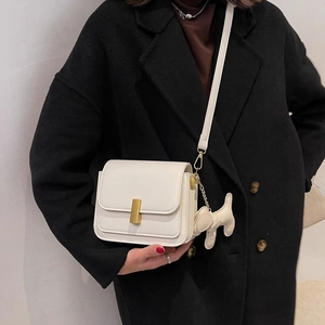 Petit sac carré blanc minimaliste avec boucle dorée et breloque chien sur manteau noir