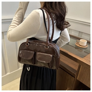 Close-up of a dark brown glossy shoulder bag with dual front pockets and top zipper