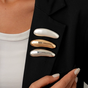 Three metallic teardrop brooches in pearl white, gold, and silver on a black blazer