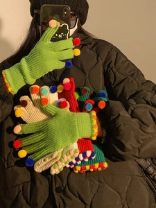 Dettaglio di guanti in maglia con pompon colorati sulle dita e polsini a costine