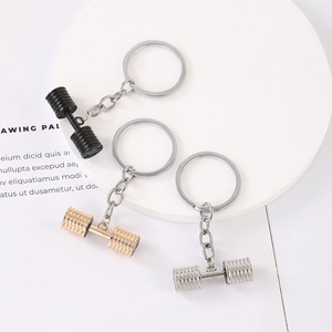 Fitness dumbbell keychains in matte black, gold, and silver finishes on white base