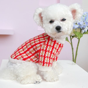 Close-up of small dog wearing red and brown plaid knit sweater in a cozy setting