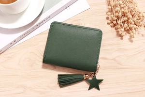 Top view of dark green pebbled leather mini wallet with tassel and star charm on a desk