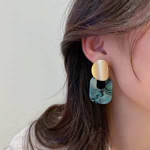Close-up of a model wearing geometric earrings with gold discs and teal marble pendants
