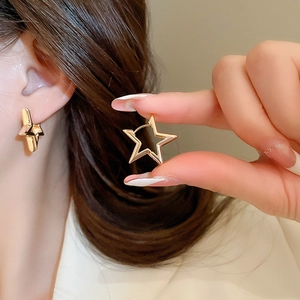 Close-up of a model wearing a gold hollow star-shaped metal earring with a polished finish