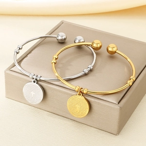 Detail of 18K gold and silver open bangles with engraved cross pendants on leather box