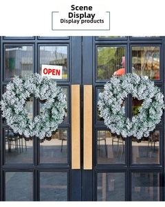 Close-up of snow-flocked Christmas wreaths hanging on black glass shop doors