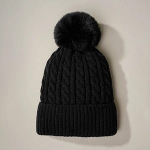 Detail of black cable knit beanie featuring a fluffy faux fur pom-pom and ribbed cuff