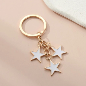 Detail of golden alloy keychain with three white enamel star-shaped pendants on peach surface