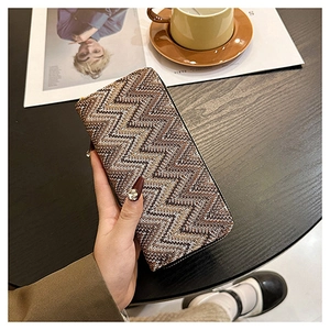 Chic long woven textured wallet in brown and gold held over a coffee table setup