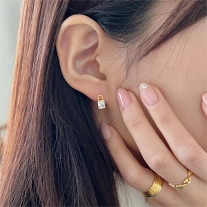 Close-up of gold square zircon padlock earring and textured layered chain rings on model
