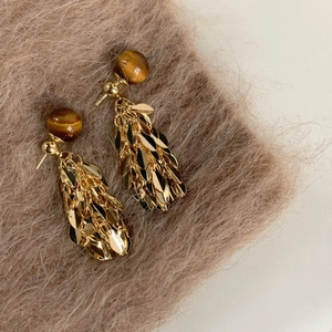Detail of golden tassel earrings with tiger eye bead and metallic leaf fringe texture