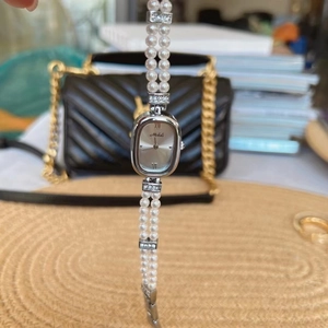 Detailaufnahme eines ovalen silbernen Zifferblatts mit zweireihigem Perlenarmband