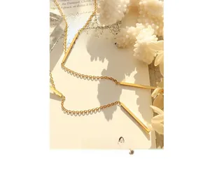Detail of 18K gold-plated Y-shaped geometric pendant on a delicate chain over vintage books