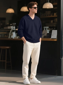 Outdoor street style shot of man in dark blue V-neck cable knit sweater with white trousers
