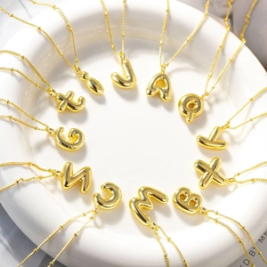 Dettaglio macro di collane con lettere 3D a palloncino e finitura a specchio oro 18K