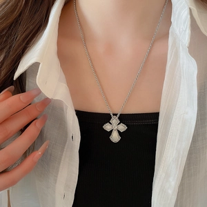 Detailed close-up of a silver cross necklace with heart element on a female model