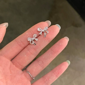 Macro shot of silver bow stud earrings with sparkling zircon stones held by hand