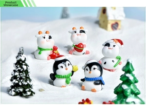 Detailed view of Christmas cow and penguin miniatures on snowy gravel with mini trees