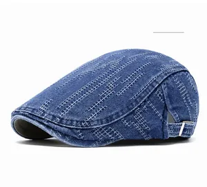 Detail of blue denim newsboy cap featuring white cross-stitch patterns and metal buckle
